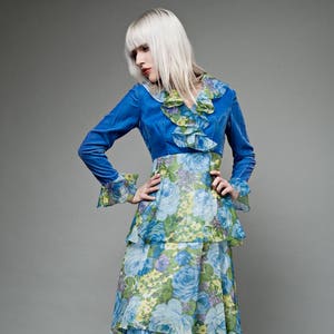 Puede incluir: Un vestido de terciopelo azul con estampado floral, cuello con volantes y falda de capas.