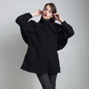 May include: A black wool coat with a large collar and a button-up front. The coat has a slightly flared silhouette and is lined with a soft, fuzzy material.