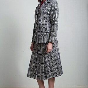 May include: A black and white checked skirt suit with a button-up skirt and a blazer. The skirt is knee-length and the blazer has a single button fastening.