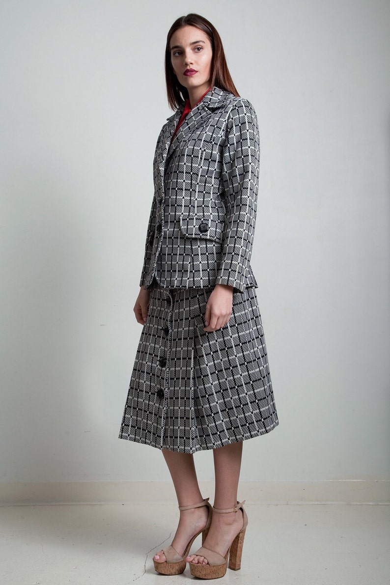 May include: A black and white checked skirt suit with a button-up skirt and a blazer. The skirt is knee-length and the blazer has a single button fastening.