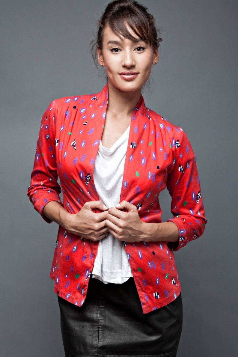 May include: A woman wearing a red and white patterned jacket with a white t-shirt and a black leather skirt.