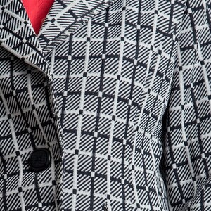 May include: Close-up of a black and white checked blazer with a button fastening. The blazer has a collar and a pocket on the right side.