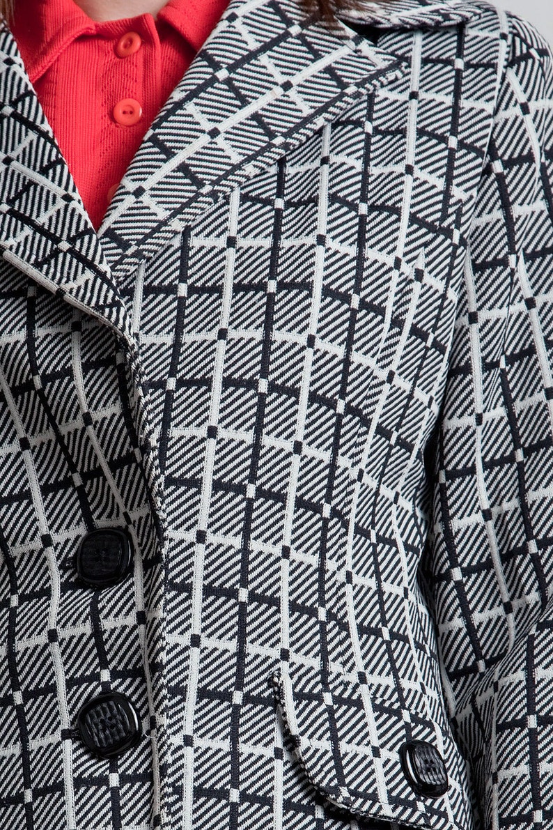 May include: Close-up of a black and white checked blazer with a button fastening. The blazer has a collar and a pocket on the right side.