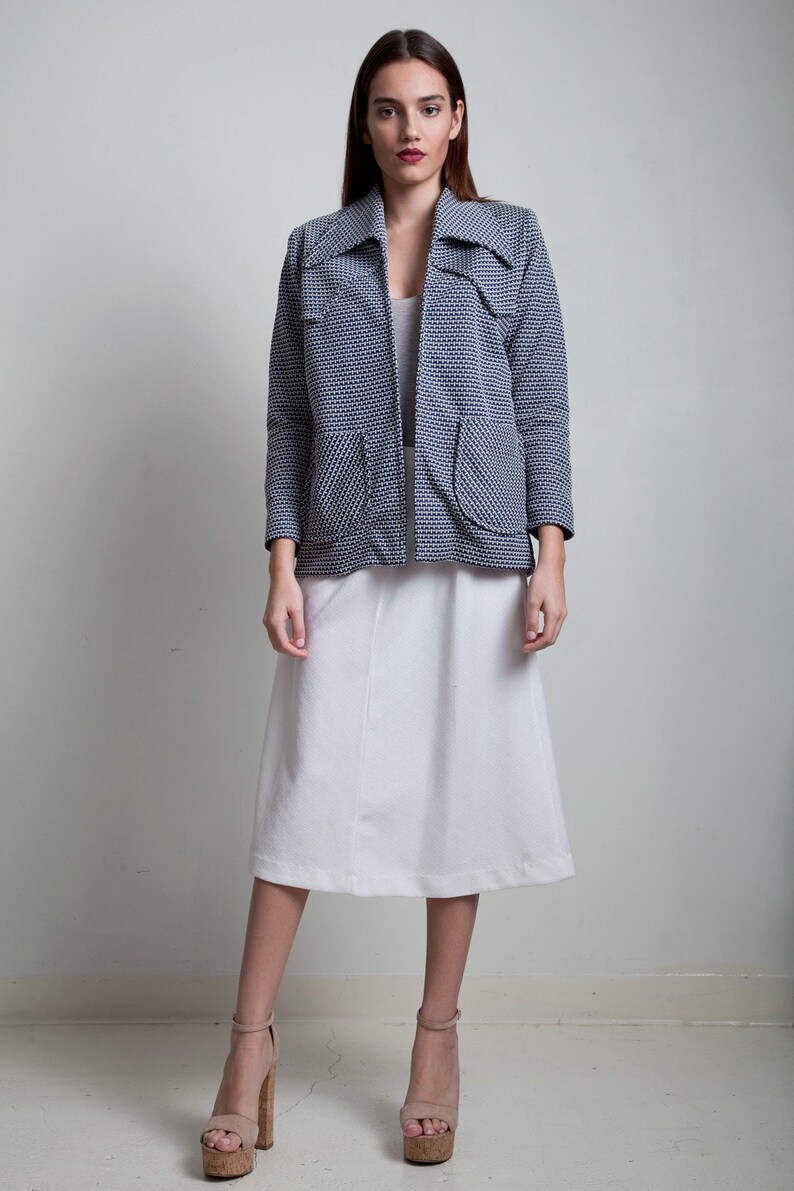 May include: A woman wearing a blue and white patterned jacket with a white skirt and cork platform sandals.