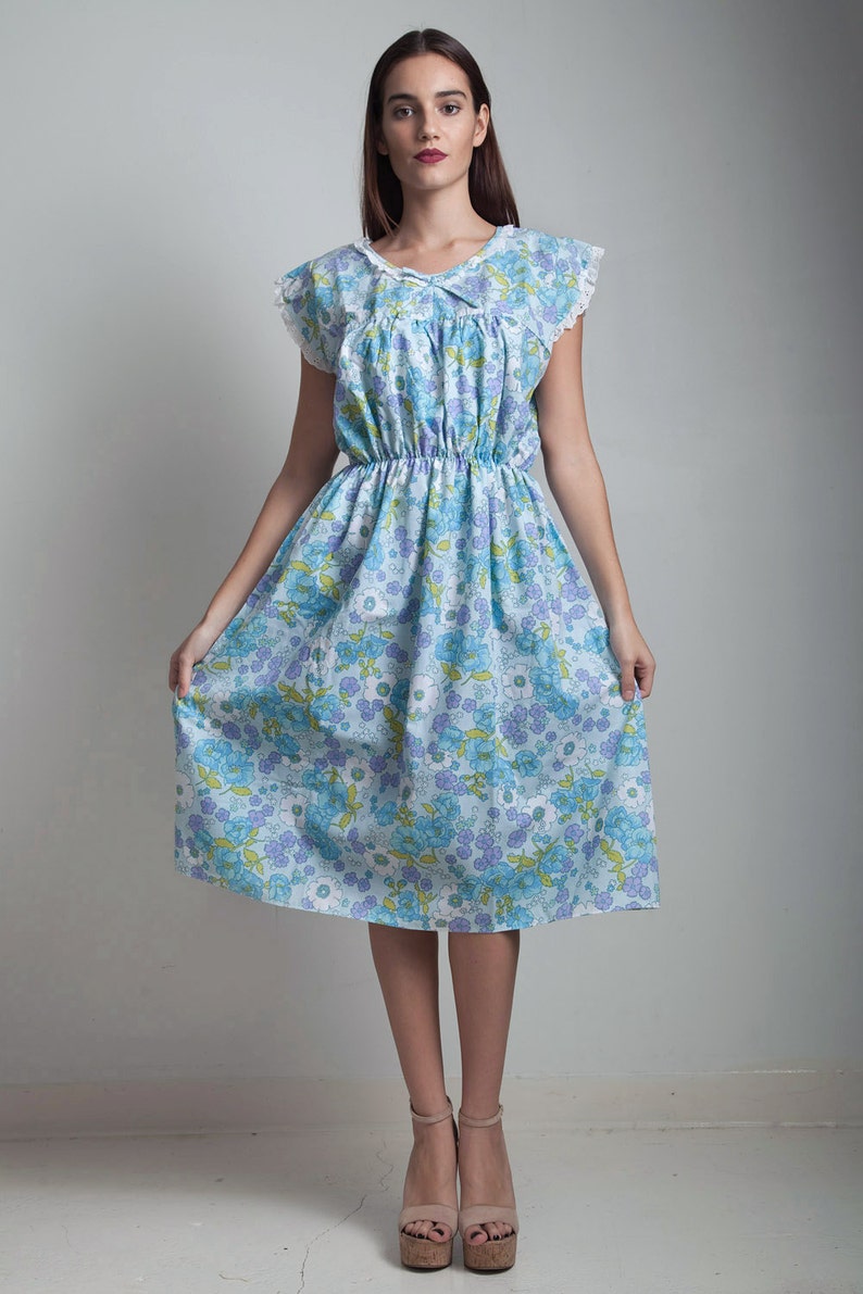 May include: A blue and white floral dress with a lace trim and a gathered waist. The dress is knee-length and has short sleeves.