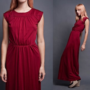 Pu&ograve; includere: Un lungo abito maxi color borgogna con una semplice scollatura rotonda e maniche corte. L'abito ha un corpetto aderente e una gonna fluida.