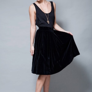 May include: A woman wearing a black tank top with a gold necklace and a black velvet skirt. She is wearing black wedge sandals with a jute platform.