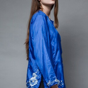 Puede incluir: Una blusa de sat&eacute;n azul con bordados florales blancos en las mangas y el dobladillo.