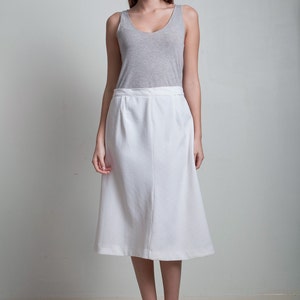 May include: A woman wearing a white skirt and a gray tank top. She is standing on a white background and wearing cork wedges.