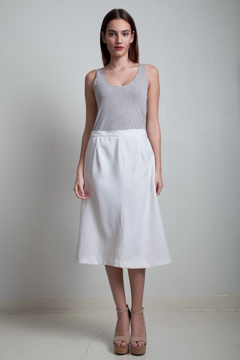 May include: A woman wearing a white skirt and a gray tank top. She is standing on a white background and wearing cork wedges.