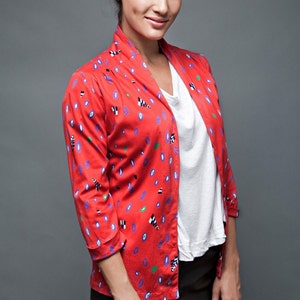 May include: A woman wearing a red, white, and blue patterned jacket over a white t-shirt and black skirt.
