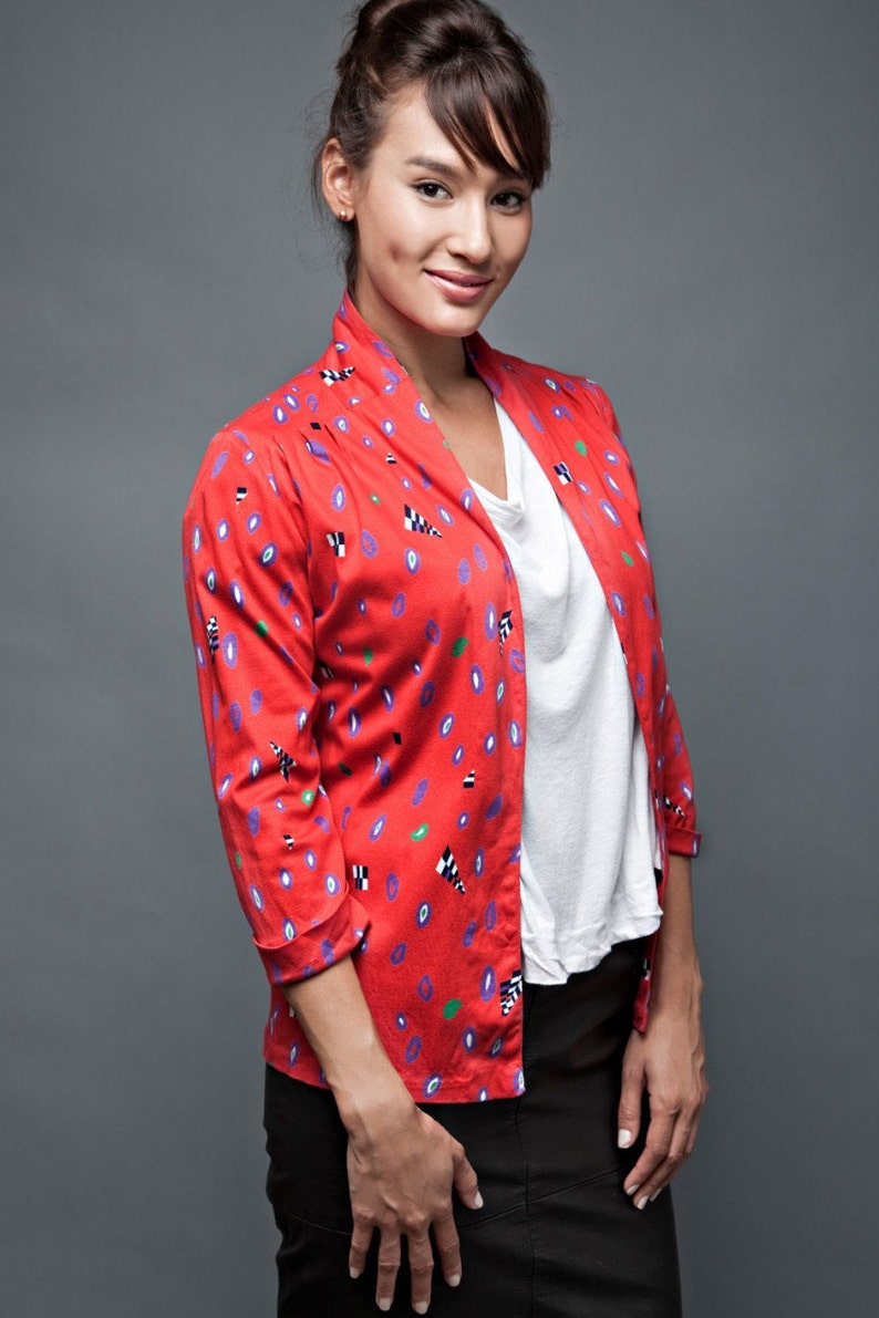 May include: A woman wearing a red, white, and blue patterned jacket over a white t-shirt and black skirt.