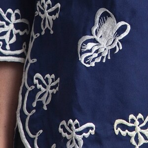 May include: A navy blue fabric with white embroidered butterflies and floral designs. The fabric has a scalloped edge.