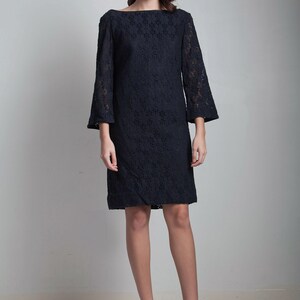 May include: A black lace dress with a boat neck and 3/4 sleeves. The dress is fitted and falls to the knee. The model is wearing nude platform heels.