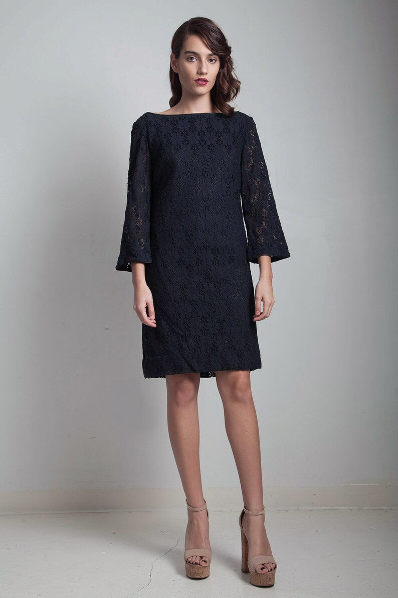 May include: A black lace dress with a boat neck and 3/4 sleeves. The dress is fitted and falls to the knee. The model is wearing nude platform heels.