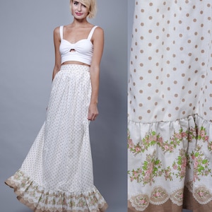 May include: A white crop top with a keyhole detail paired with a long, flowing skirt. The skirt features a cream background with small brown polka dots and a floral and lace trim at the hem. The skirt's length is approximately 40 inches.