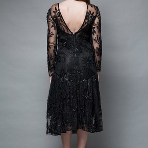 May include: A black lace dress with long sleeves and a low back. The dress has a fitted bodice and a flowing skirt.