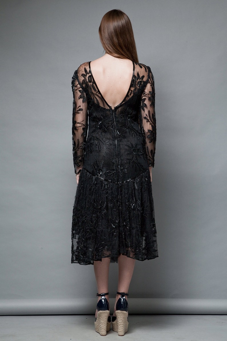 May include: A black lace dress with long sleeves and a low back. The dress has a fitted bodice and a flowing skirt.