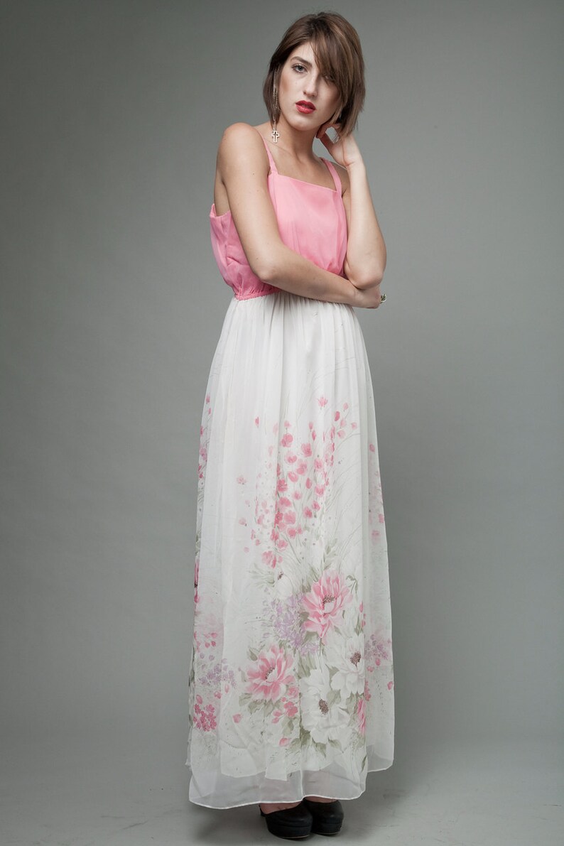 May include: A woman wearing a pink and white floral maxi dress. The dress has a pink bodice and a white skirt with pink floral print.