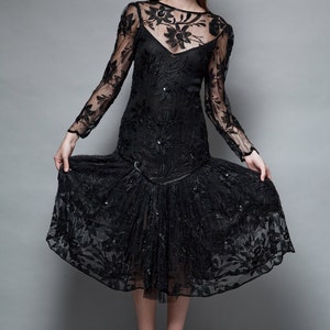 May include: A black lace dress with a floral pattern and a ruffled hem. The dress has long sleeves and a scoop neckline.
