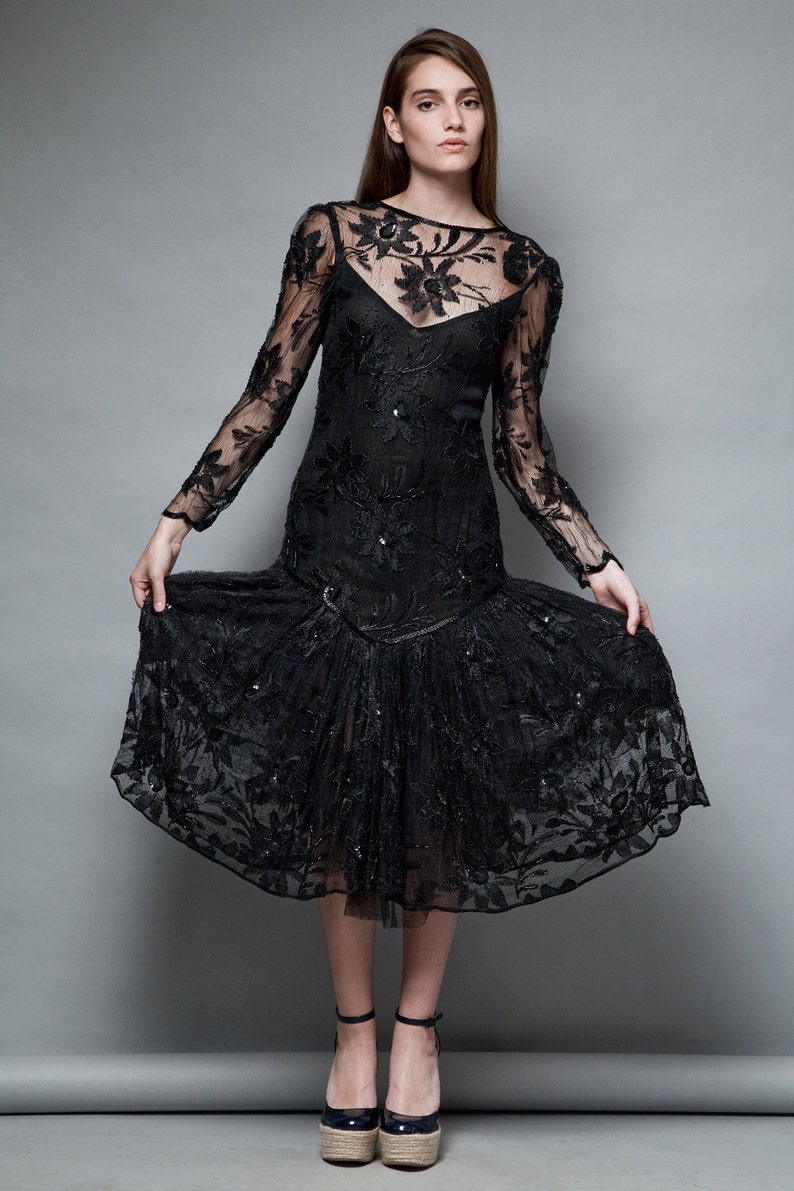 May include: A black lace dress with a floral pattern and a ruffled hem. The dress has long sleeves and a scoop neckline.