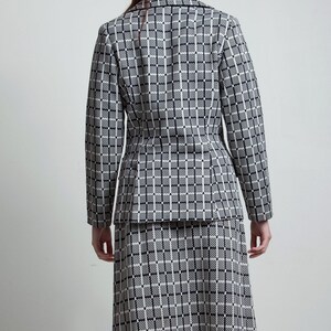May include: A black and white checked blazer and skirt set. The blazer has a notched collar and long sleeves. The skirt is knee-length and has a straight silhouette.