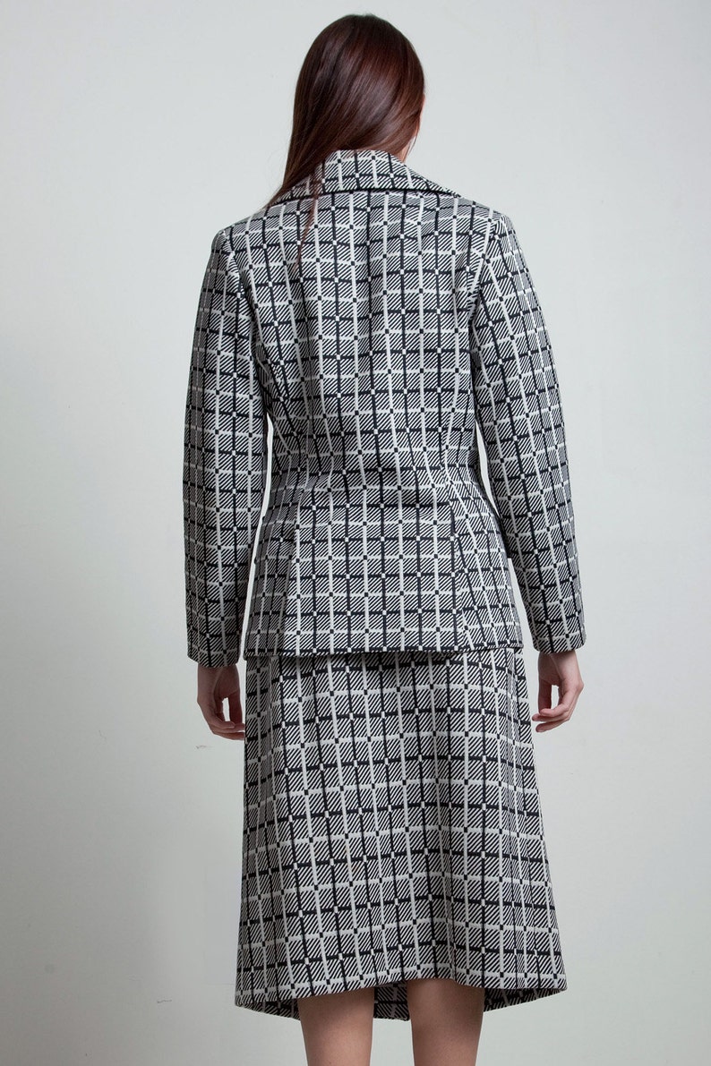 May include: A black and white checked blazer and skirt set. The blazer has a notched collar and long sleeves. The skirt is knee-length and has a straight silhouette.