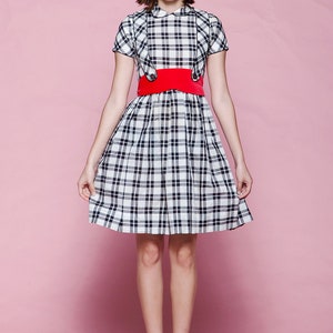 May include: A plaid dress with a red belt and red shoes. The dress features a black and white plaid pattern, a white collar, and short sleeves. The red belt cinches the waist, and the shoes are a matching red color.