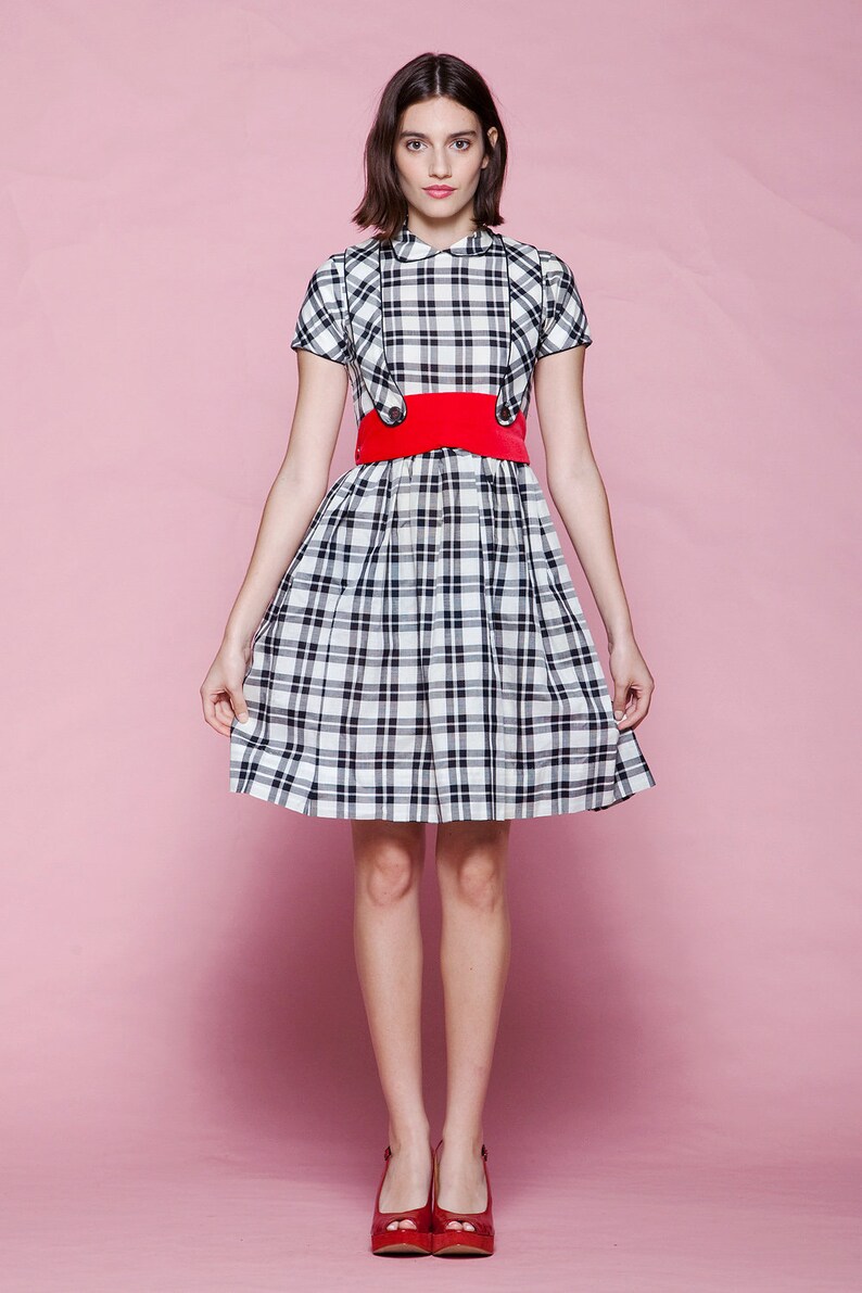 May include: A plaid dress with a red belt and red shoes. The dress features a black and white plaid pattern, a white collar, and short sleeves. The red belt cinches the waist, and the shoes are a matching red color.