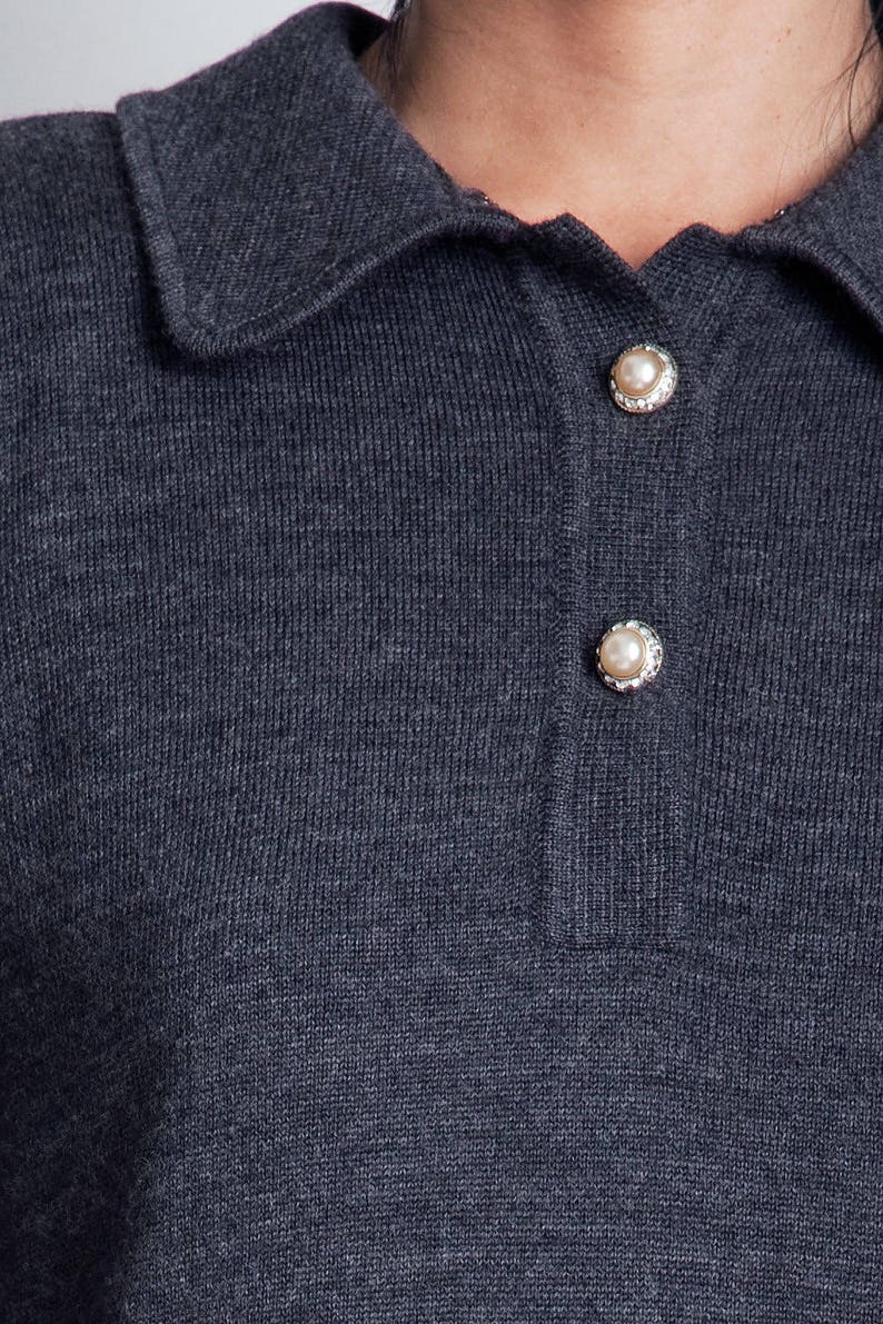 May include: A dark gray knitted collared shirt with pearl buttons.