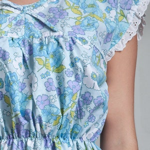 May include: A light blue dress with a floral print featuring blue and purple flowers. The dress has a gathered waist and a white lace trim on the sleeves.