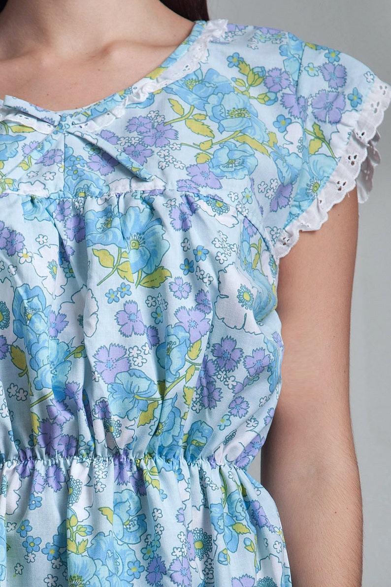 May include: A light blue dress with a floral print featuring blue and purple flowers. The dress has a gathered waist and a white lace trim on the sleeves.