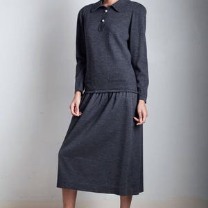 May include: A charcoal gray knit dress with a collared neckline and long sleeves. The dress has a gathered waist and a midi length skirt.