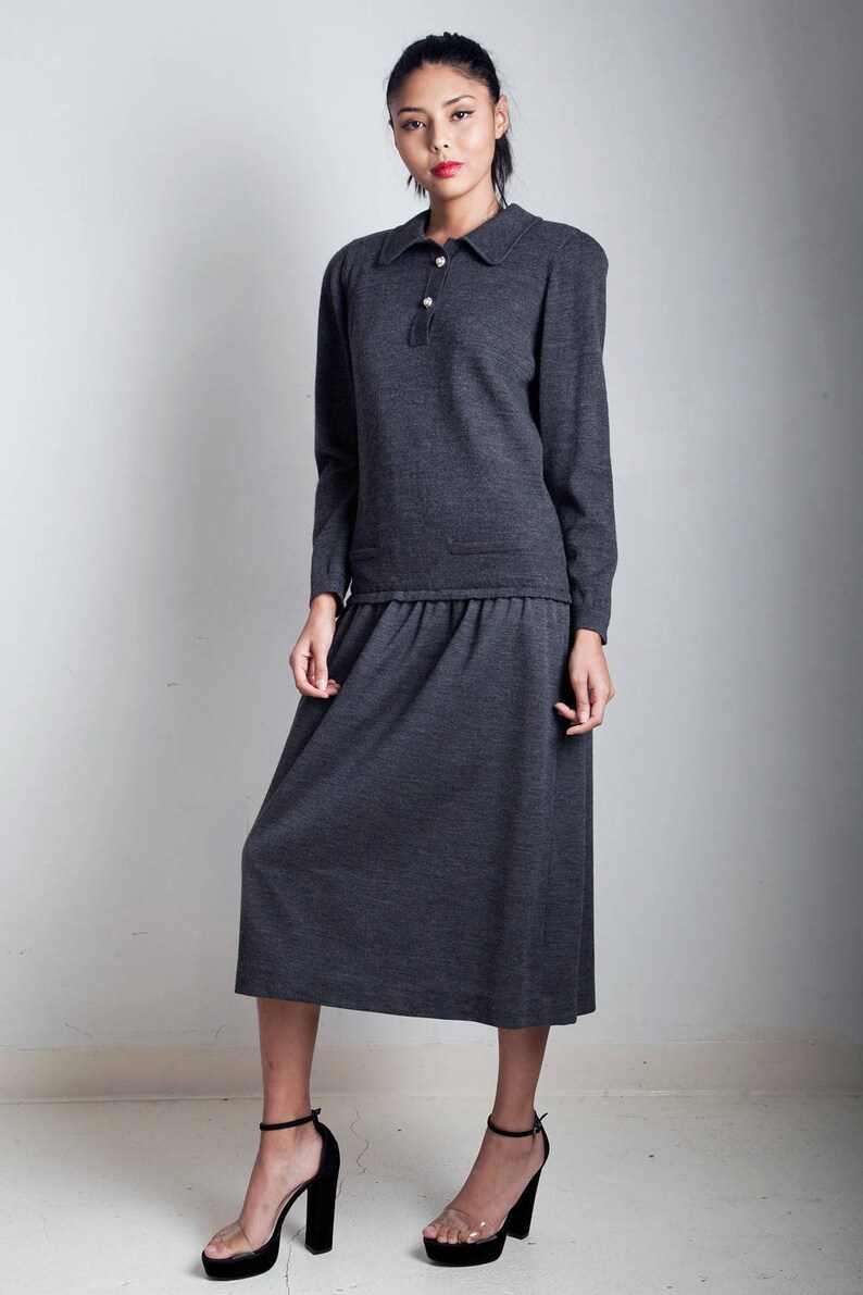 May include: A charcoal gray knit dress with a collared neckline and long sleeves. The dress has a gathered waist and a midi length skirt.