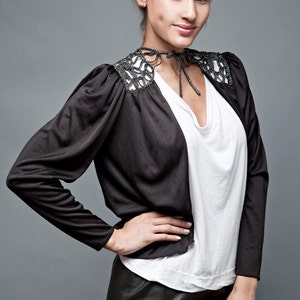 May include: A woman wearing a black cropped jacket with a beaded collar, a white t-shirt, and a black leather skirt.