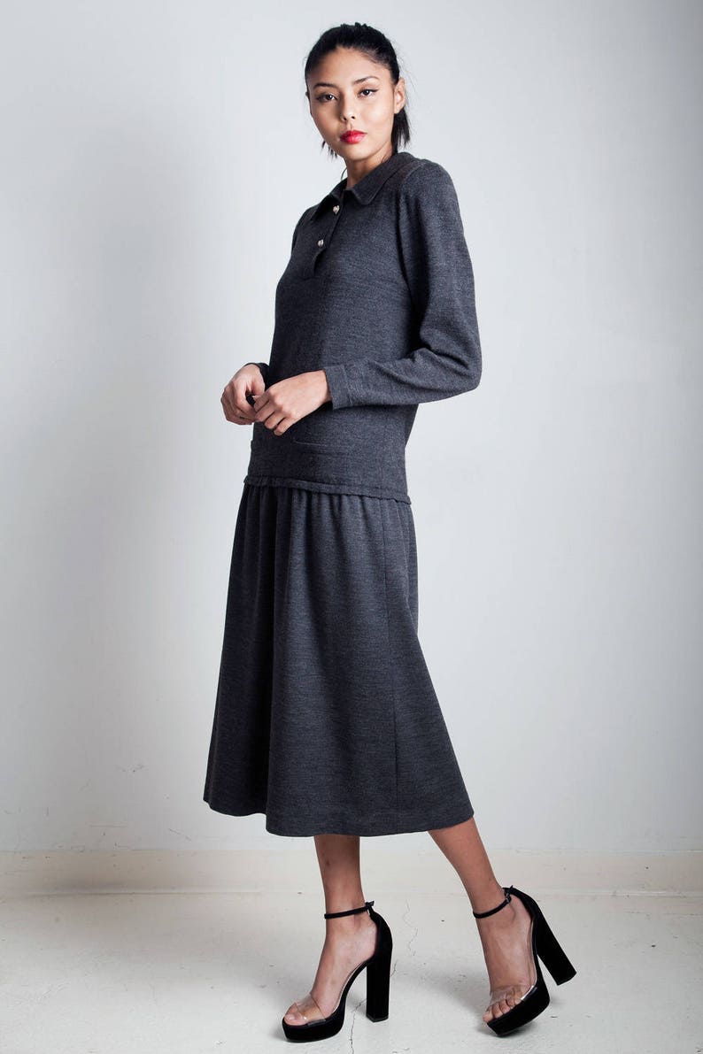 May include: A charcoal gray long-sleeved dress with a collared neckline and a gathered waist. The dress is made of a soft, knit fabric and has a relaxed fit. The model is wearing black heeled sandals.