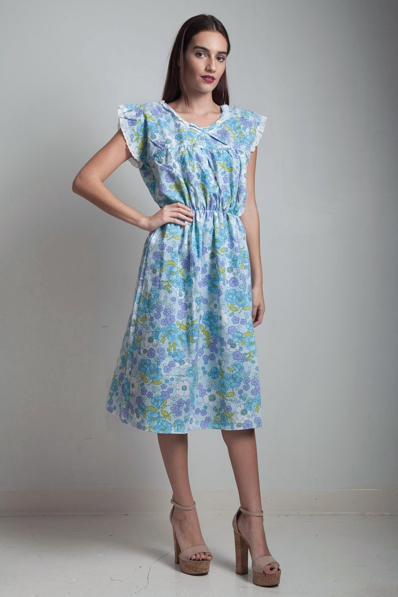 May include: A blue and white floral dress with a white lace trim on the sleeves. The dress has a cinched waist and a knee-length skirt.