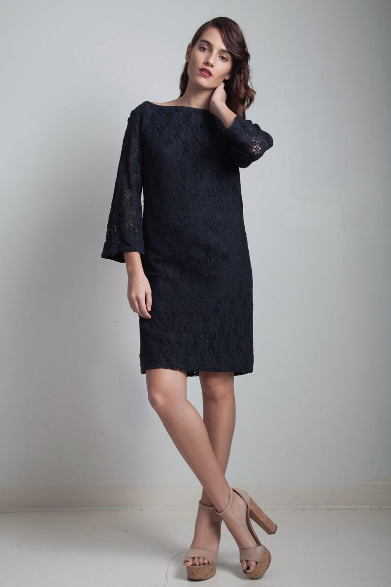 May include: A black lace dress with a boat neck and 3/4 sleeves. The dress is fitted and falls to the knee. The model is wearing nude heels.