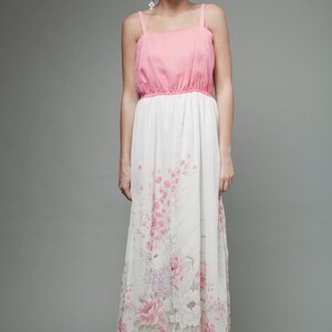 May include: A woman wearing a pink and white maxi dress with a floral print. The dress has a fitted bodice and a flowing skirt.
