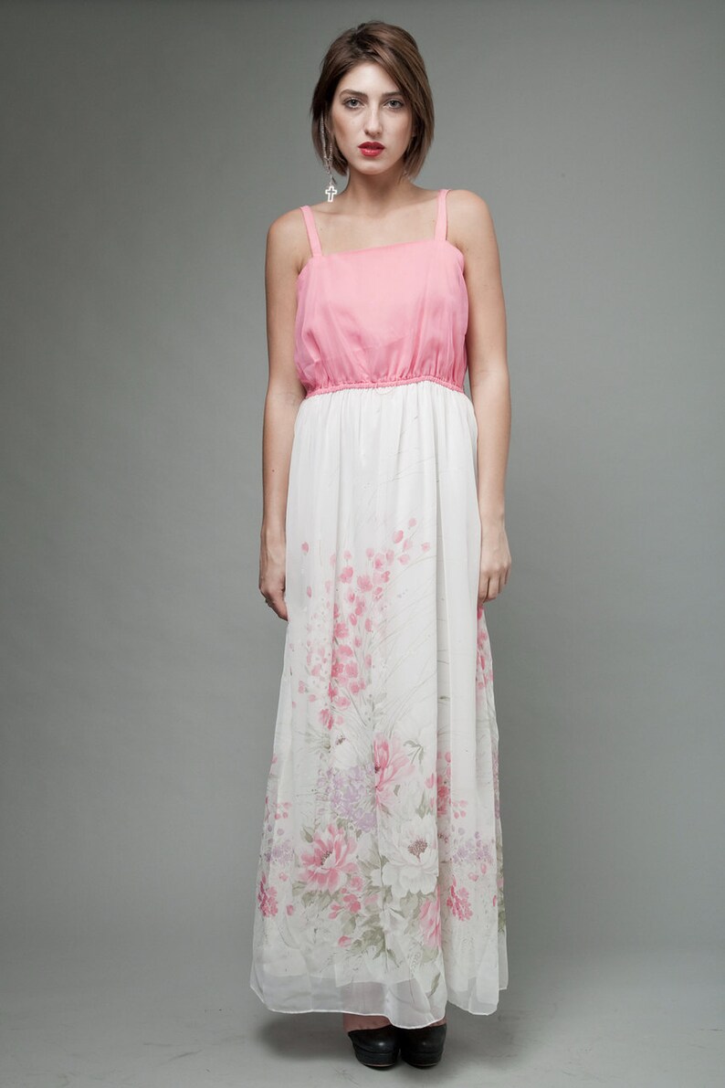 May include: A woman wearing a pink and white maxi dress with a floral print. The dress has a fitted bodice and a flowing skirt.