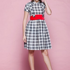 May include: A black and white plaid dress with a red belt and red heels. The dress has a Peter Pan collar and short sleeves. The belt is wide and cinches the waist. The heels are open-toe and have a unique wedge design.