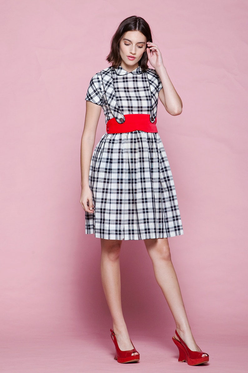 May include: A black and white plaid dress with a red belt and red heels. The dress has a Peter Pan collar and short sleeves. The belt is wide and cinches the waist. The heels are open-toe and have a unique wedge design.