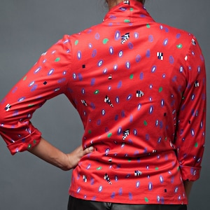 May include: A red long-sleeved shirt with a geometric pattern in shades of purple, green, black, and white.