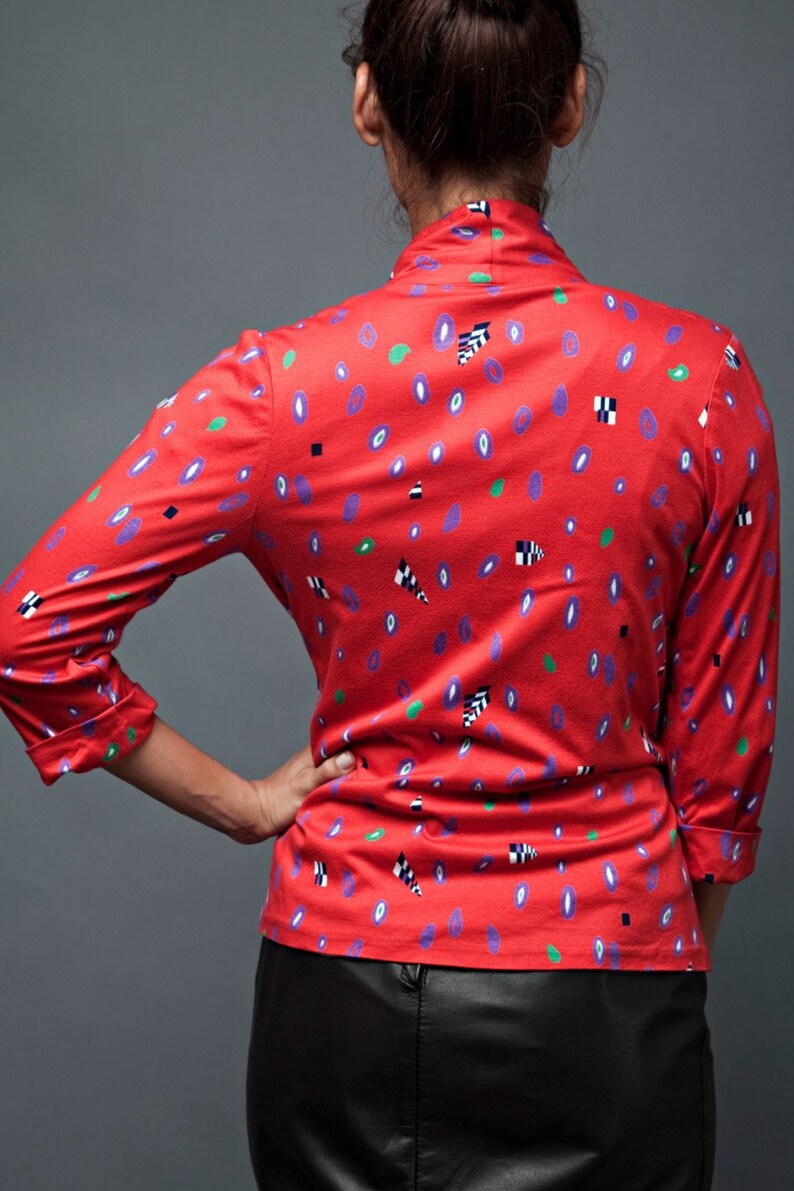 May include: A red long-sleeved shirt with a geometric pattern in shades of purple, green, black, and white.