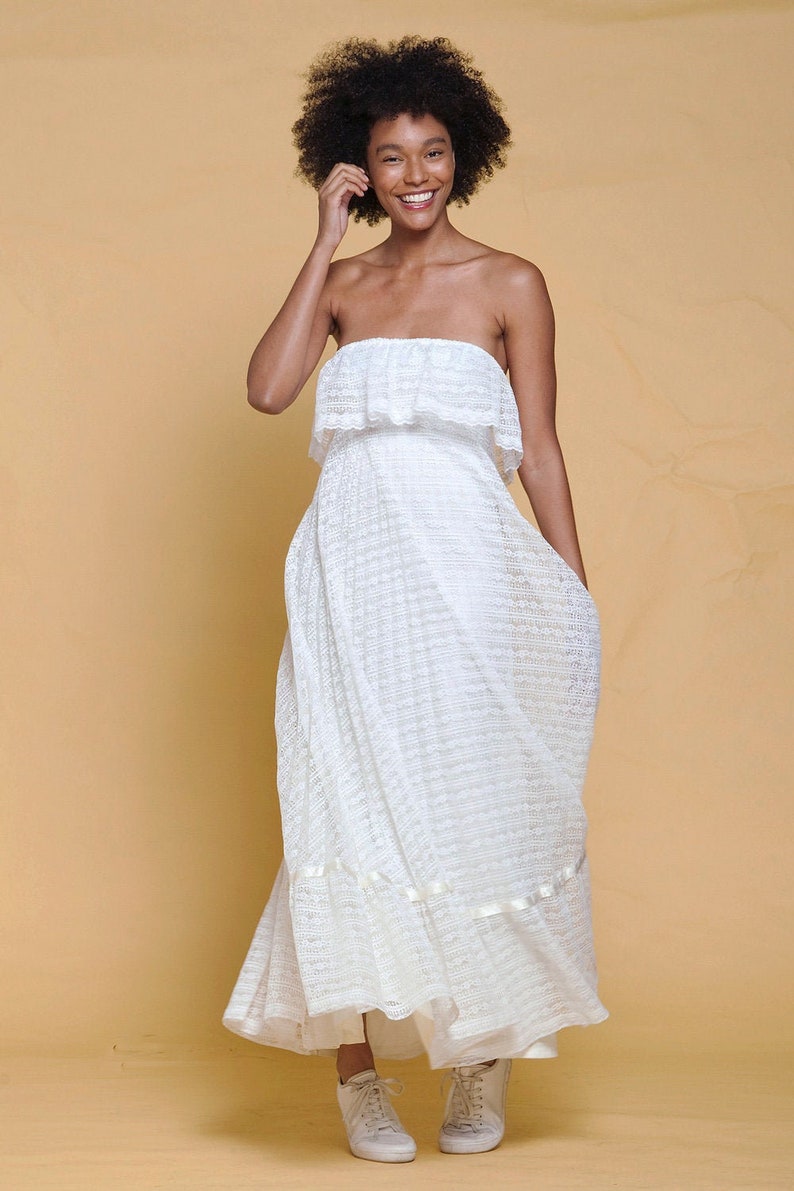 Puede incluir: Una mujer con un vestido blanco de tirantes sin tirantes y un estampado de encaje blanco. Ella sonr&iacute;e y lleva zapatillas blancas.
