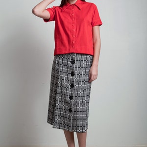 May include: A red short-sleeved button-down shirt with a black and white plaid skirt. The skirt has a button-down front.