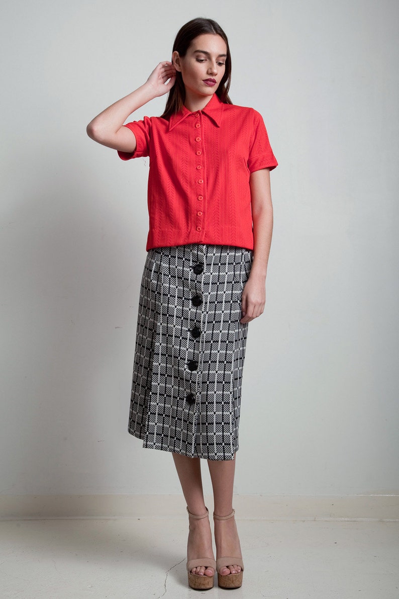 May include: A red short-sleeved button-down shirt with a black and white plaid skirt. The skirt has a button-down front.