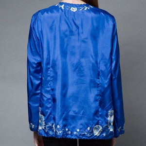 Puede incluir: Una chaqueta de sat&eacute;n azul real con detalles florales bordados en blanco alrededor del cuello y el dobladillo.