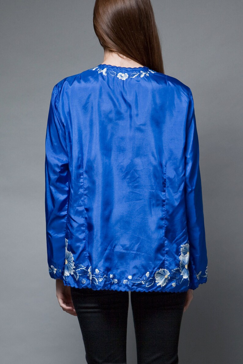 Puede incluir: Una chaqueta de sat&eacute;n azul real con detalles florales bordados en blanco alrededor del cuello y el dobladillo.