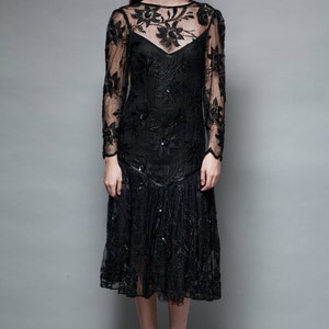 May include: A black lace dress with floral embroidery and a ruffled hem. The dress has long sleeves and a round neckline.